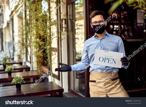 stock-photo-happy-waiter-with-protective-face-mask-holding-open-sign-while-standing-at-cafe-doorway-1742687024